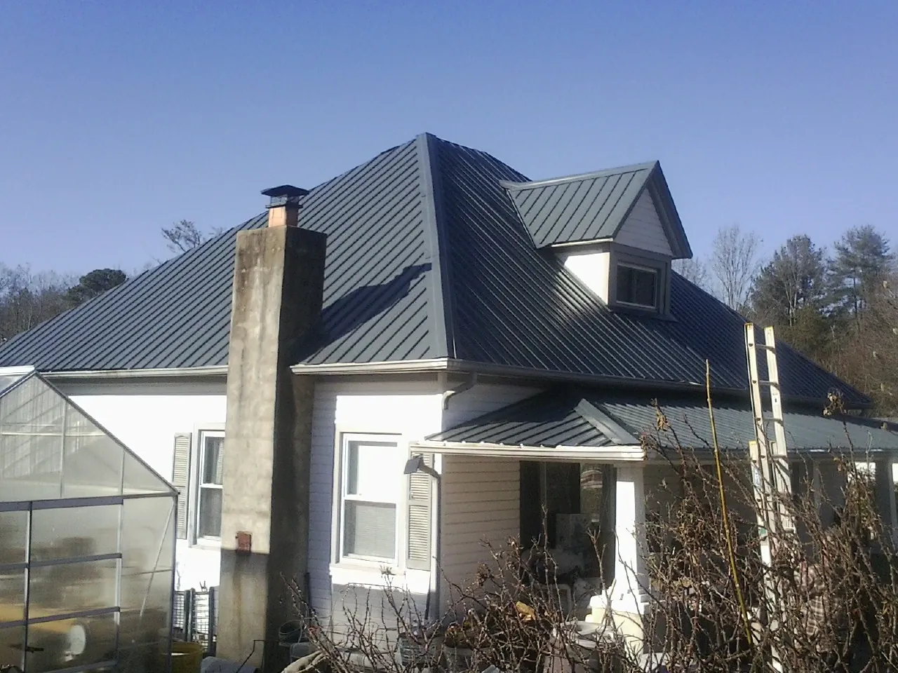 Dark blue standing seam metal roof on a white farmhouse with dormer — Slate & Tile Roof Repair by Roofing Brothers in Miles City