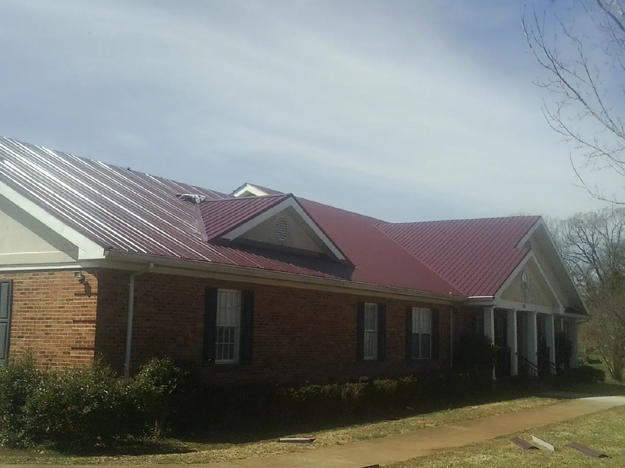 Red metal roof with gabled entries on a long brick building, from a Hail Damage Roof Repair job in Miles City