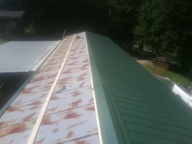 Old rusted panels beside newly installed green metal roofing — Wind Damage Roof Repair by Roofing Brothers in Miles City