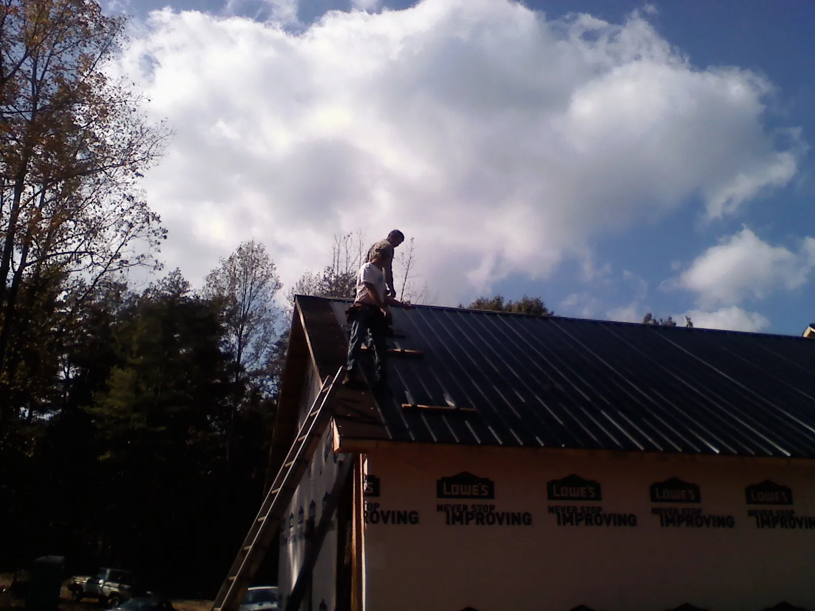 Roofer fastening dark metal panels high against a cloudy sky in Miles City
