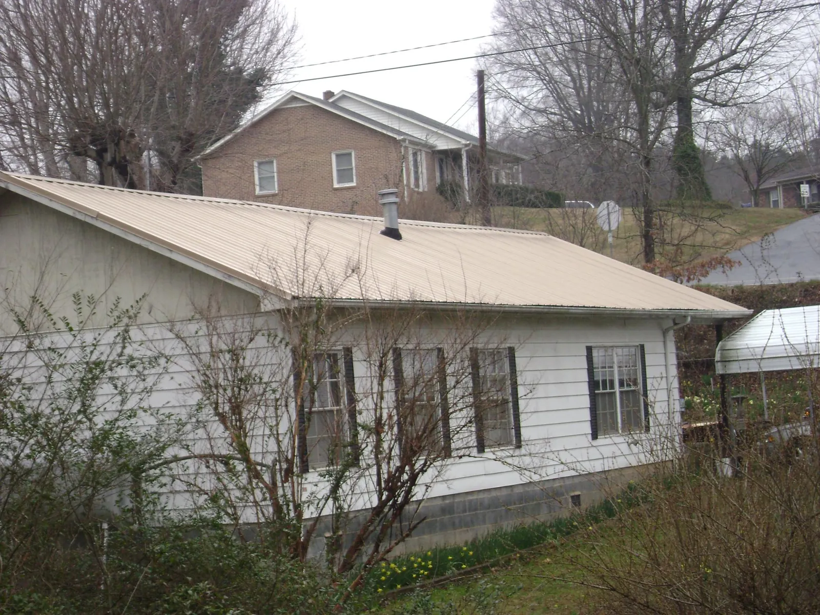 Tan metal roof on a white sided house set into a hillside — Commercial Roofing by Roofing Brothers in Miles City